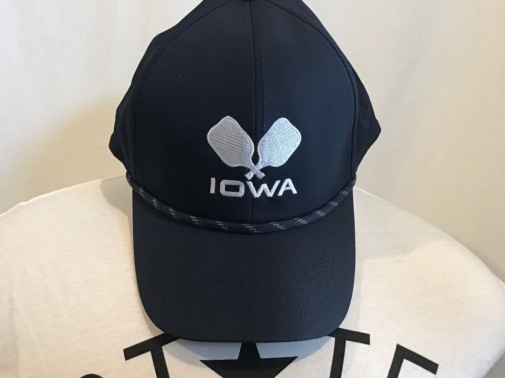 A navy blue baseball hat with a navy rope across the top brim featuring two white crossed pickleball paddles with IOWA embroidered at the front center