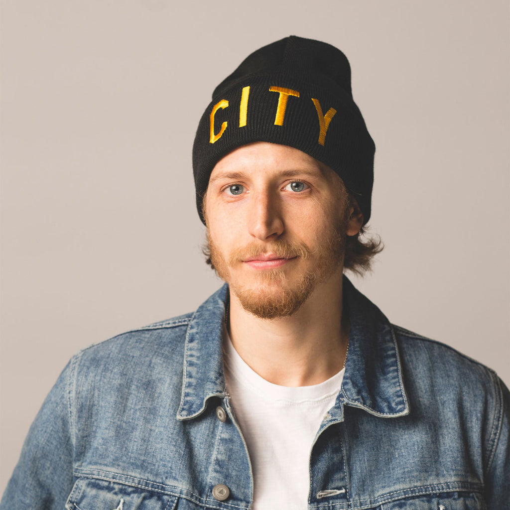 blonde haired blue eyed male model wearing black beanie with folding cuff in cuff city embroidered in gold