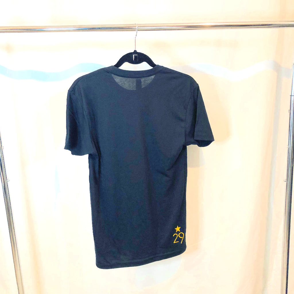 a black t-shirt hanging from a hanger on a rack the back of the shirt has the 29th state apparel logo on the lower left corner