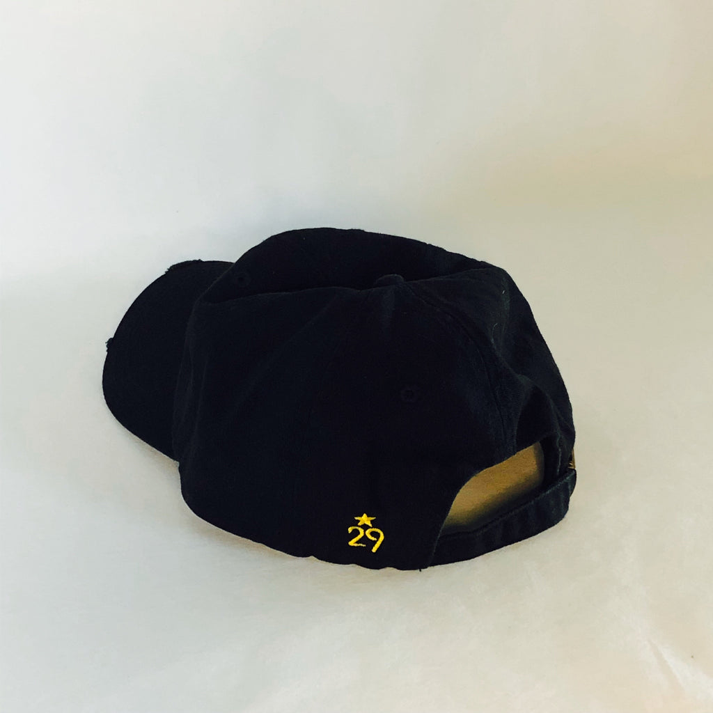 back of the all black dad hat showcasing the 29th state apparel logo embroidered in gold thread on the back left panel near the adjustable slide closure