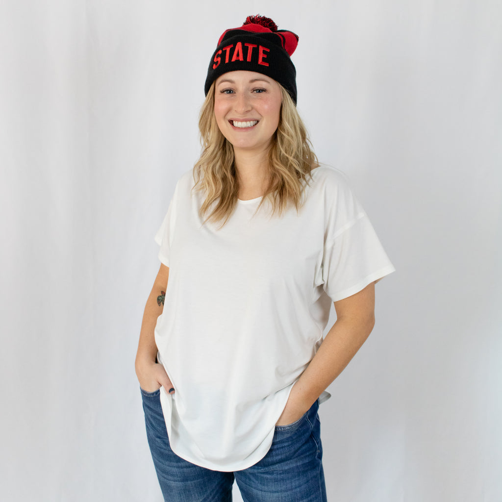shoulder length blonde haired young woman smiling in a two-tone black and red striped beanie state in red on front fold